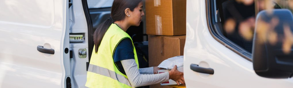 A delivery person in a high-visibility vest is handling packages from the back of a white van.